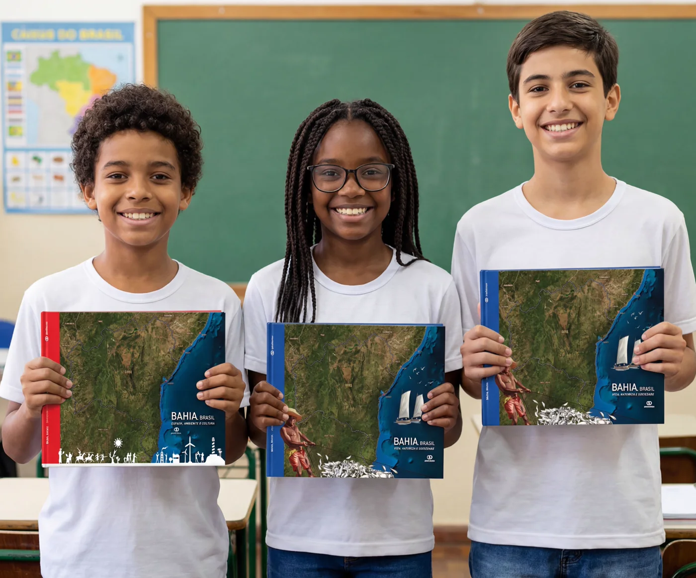 Três estudantes da rede sorrindo, cada um segurando um exemplar do livro territorializado da Bahia, com o mapa de satélite do território na capa